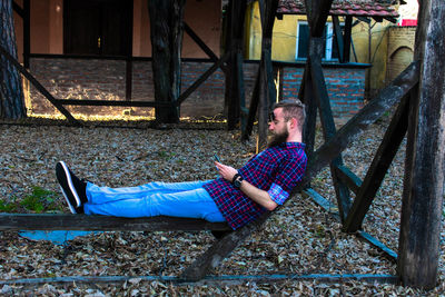 Full length of man using phone while sitting on wood