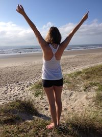 Rear view of woman with arms raised standing at beach