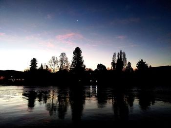 Silhouette trees by lake against sky during sunset