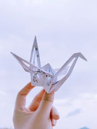 Cropped hand holding origami against cloudy sky