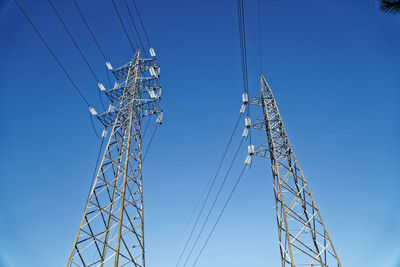Low angle view of electricity pylon against blue sky