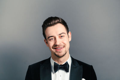 Portrait of happy young man wearing tuxedo against gray background
