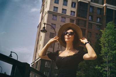 A pretty charming middle-aged woman in a black dress, hat and sunglasses strolls through the street