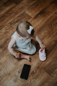 High angle view of girl sitting on wooden floor with shoe and mobile phone
