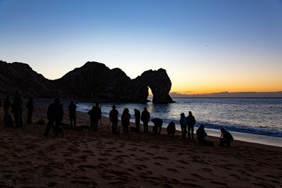 Silhouette people on beach against clear sky during sunset