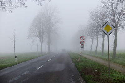 Road sign by trees against sky during foggy weather