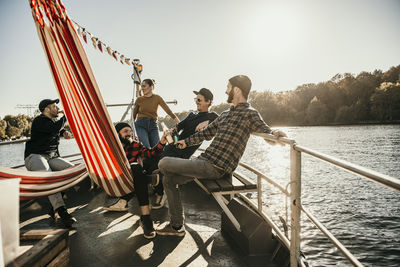 Happy friends spending leisure time together sitting on boat on sunny day