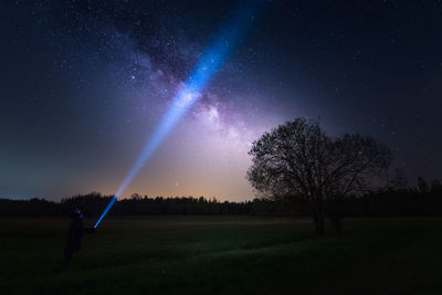 Silhouette view of person holding a flaslight illuminating the night sky and the milky way