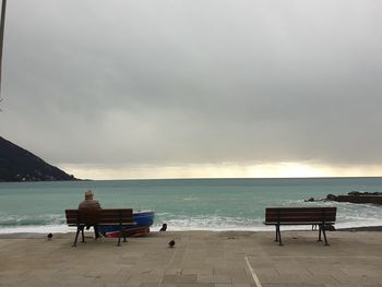 Rear view of people sitting on bench at beach against sky