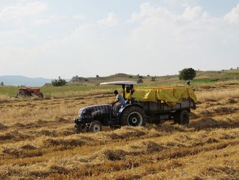 Farmer with agricultural machinery on field against sky