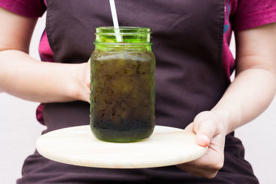 Midsection of woman holding cutting board with mason jar against white background