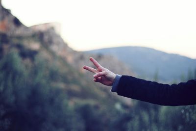 Close-up of human hand in peace sign against the sky