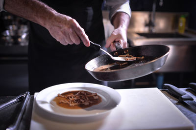 Midsection of chef serving cooked mushrooms in plate at commercial kitchen