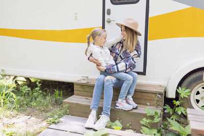Mother and daughter sitting on steps against bus
