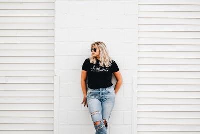 Young woman looking away while standing against white wall