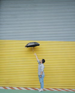Side view of man with umbrella standing by closed shutter