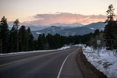 Empty country road amidst trees against sky during sunset