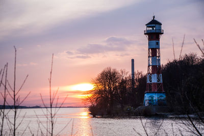 Lighthouse by sea against sky during sunset