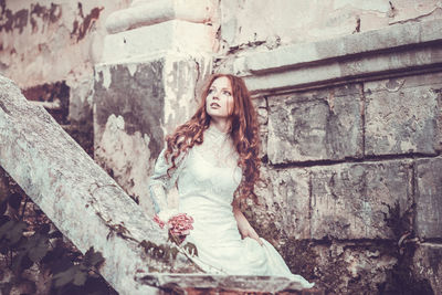 Portrait of a young woman standing against stone wall