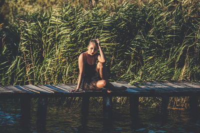 Young woman sitting on wood against trees