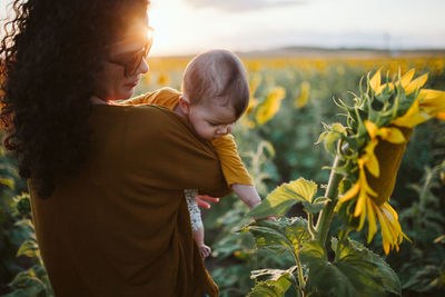 Rear view of mother carrying toddler son at sunflower farm during sunset