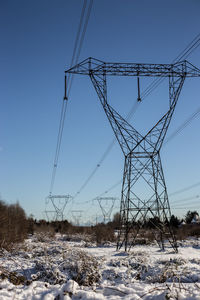 Electricity pylon on snowy field against sky