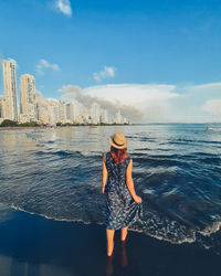 Rear view of woman standing on rock by sea against sky
