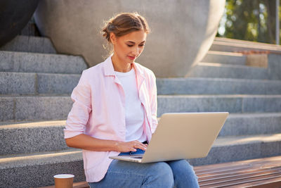 Young woman using mobile phone while sitting on staircase