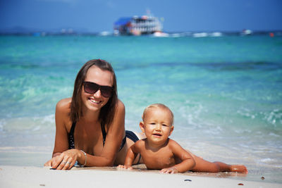 Portrait of smiling young woman sitting on beach against sky