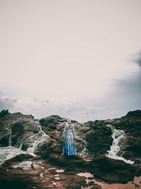 Rear view of person standing on rocks against sky