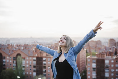 Young man with arms outstretched standing against cityscape