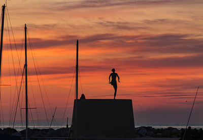 Silhouette man standing on beach against orange sky