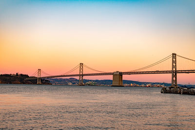 Suspension bridge over river against sky during sunset