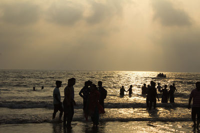 People at beach against sky during sunset