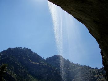 Low angle view of waterfall and mountains against clear blue sky