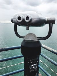 Close-up of coin-operated binoculars by sea against sky
