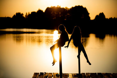 Silhouette people by lake against sky during sunset