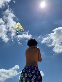 Rear view of boy flying kite standing against sky
