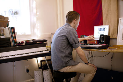 Side view of man with piano using laptop computer