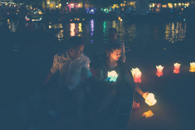 Couple holding illuminated decoration while sitting in boat on lake