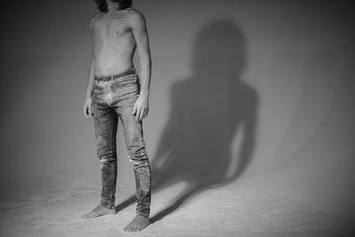Low section of shirtless man while standing over white background