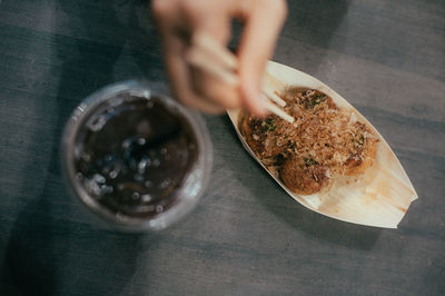 Cropped hands eating takoyaki using chopsticks on table
