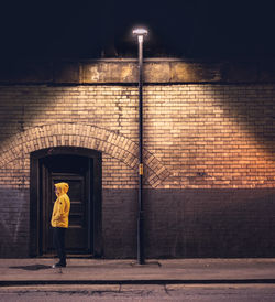 Side view full length of woman standing outside building on sidewalk at night