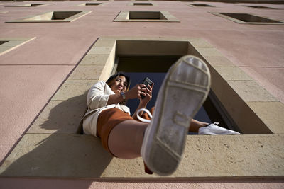 Asian woman with mobile phone sitting on window sill of building