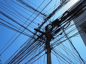 Low angle view of electricity pylon against clear blue sky