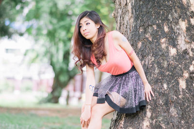 Beautiful young woman against tree trunk