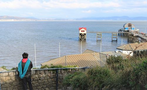 Rear view of people looking at sea and pier against sky