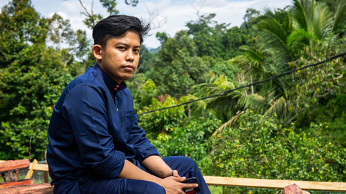 Young man sitting against trees
