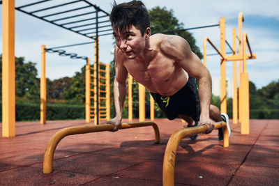 Full length of shirtless young man exercising at playground