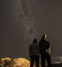 Rear view of people standing against star field at night